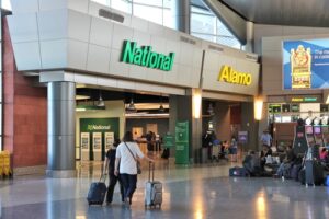 Travelers with luggage walking past the National Car Rental counter inside an airport terminal