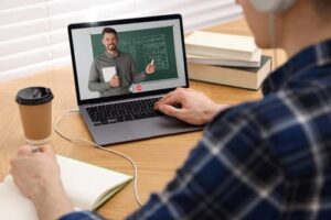 Person watching an online course on a laptop while taking notes