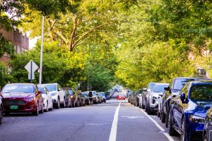 Cars parked along both sides of a leafy residential street in a U.S. city, showing legal curbside parking.