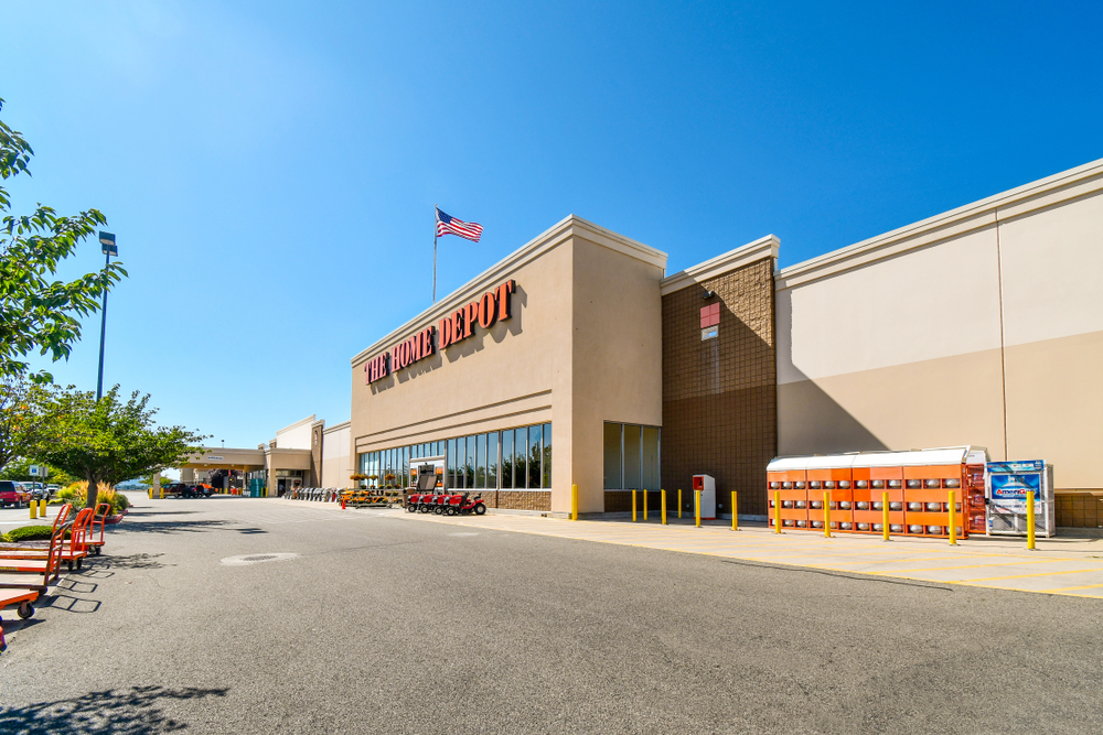 Wide exterior view of a Home Depot store with an American flag, shopping carts, and a clear blue sky.