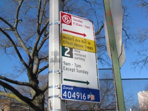 A New York City street sign showing alternate side parking hours, a street-cleaning rule for Tuesday from 9:30 to 11 AM, and 2-hour metered parking rules from 9 AM to 7 PM except Sunday.